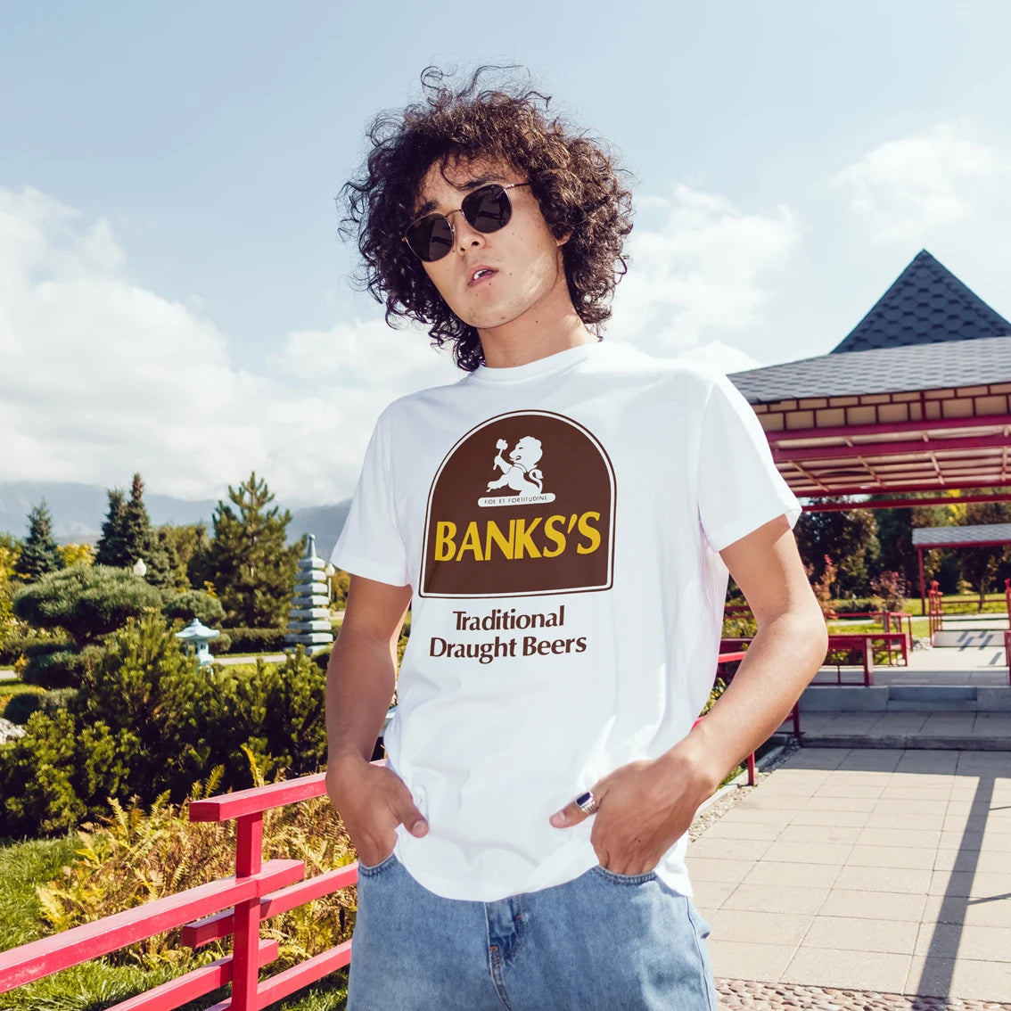 A man in sunglasses is wearing a white t-shirt with 'Banks's Traditional Draught Beers' logo outdoors.