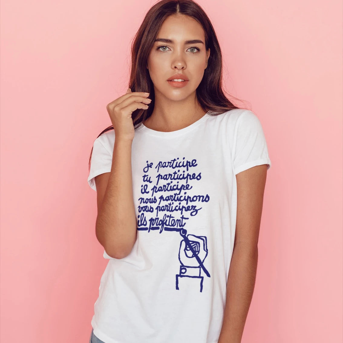 A woman is wearing a white t-shirt with 'JE PARTICIPE' blue texts and the picture of a writing hand against a pink background
