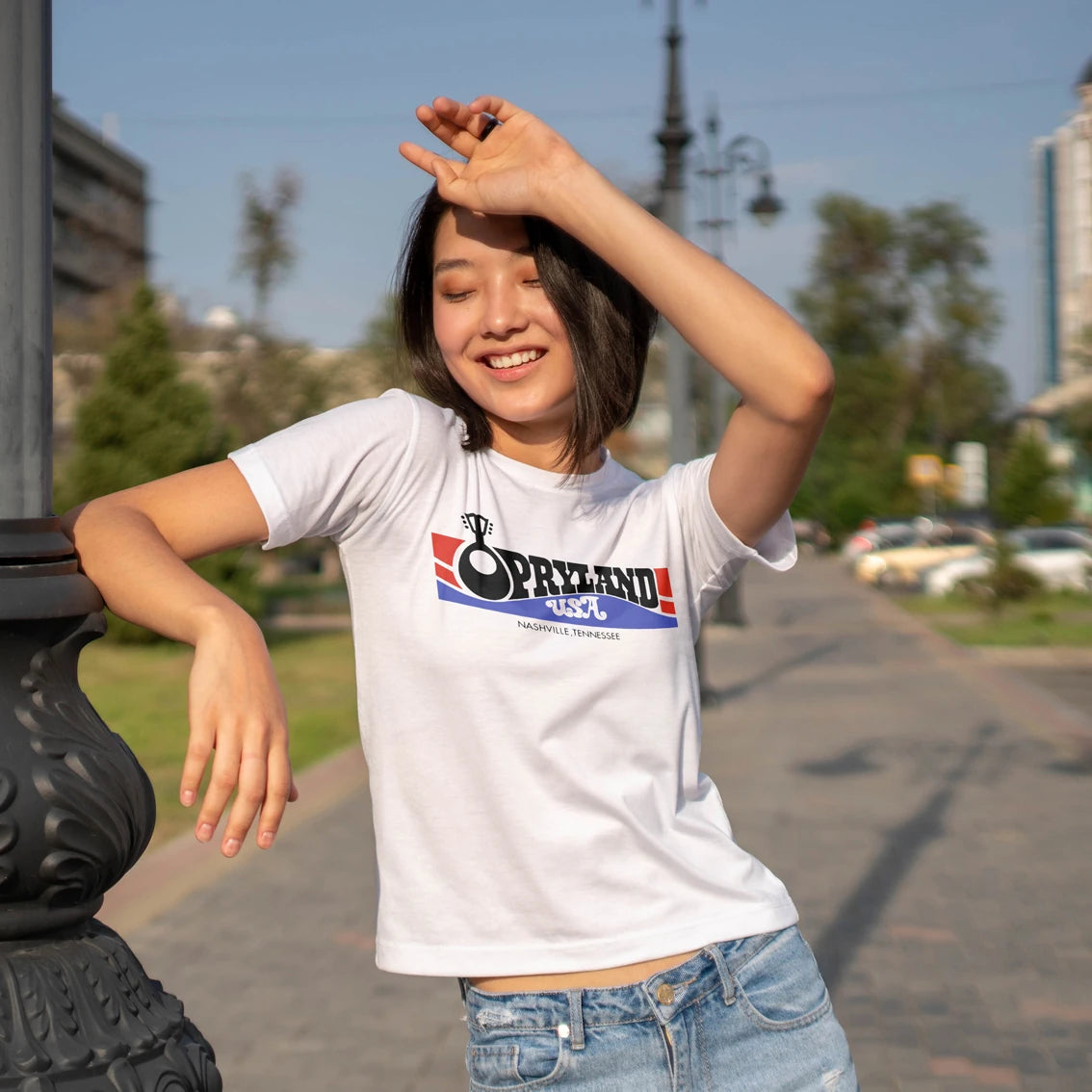Woman wearing a white t-shirt with a 'Opryland USA' logo, standing outdoors on a sunny day.