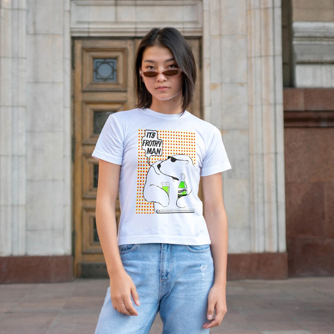 Woman wearing a white t-shirt with a graphic design of bear holding soft drink and text saying 'It's Frothy Man' in front of a building