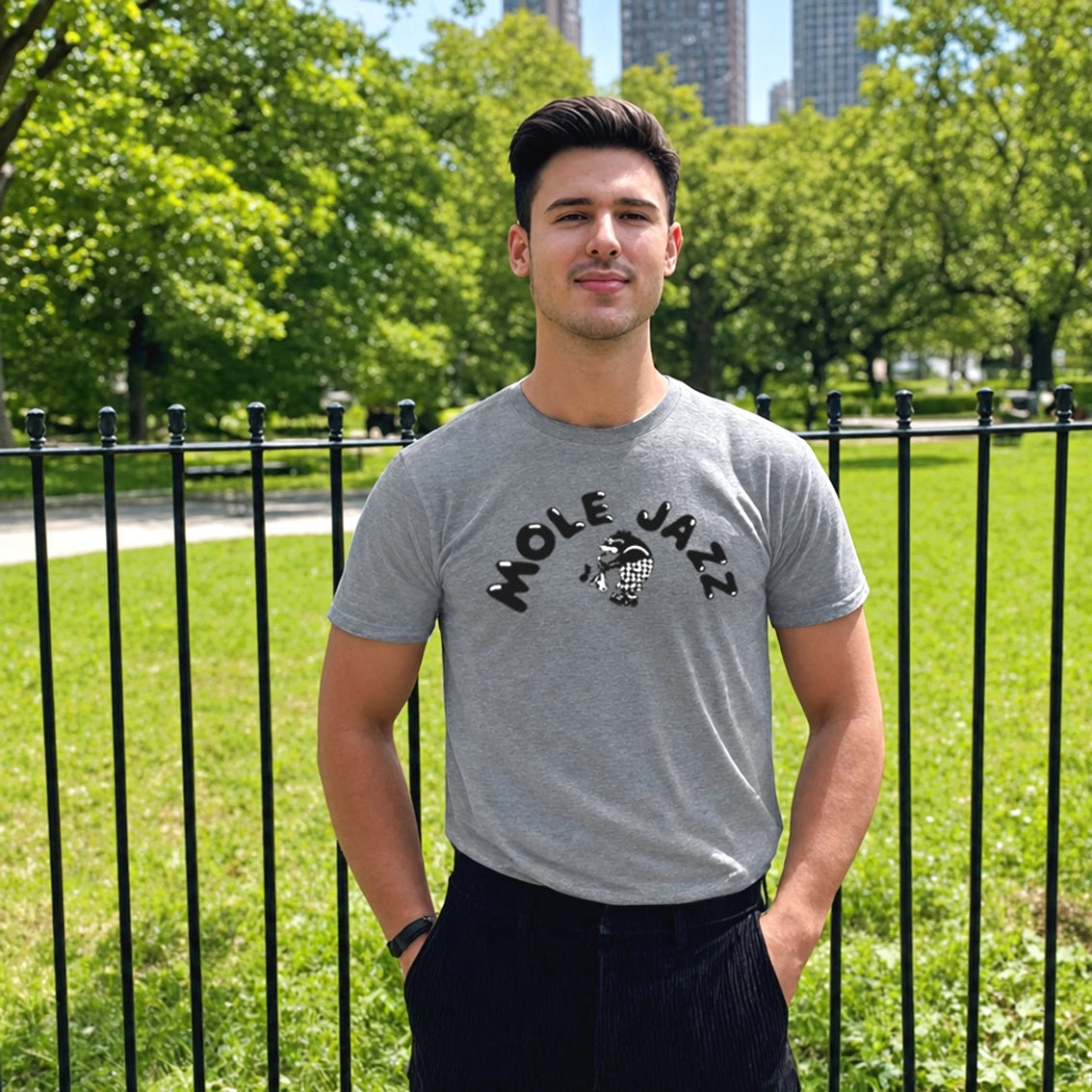 Man standing in front of an urban grassy area wearing a grey t-shirt with the words Mole Jazz and a picture of a mole playing saxophone