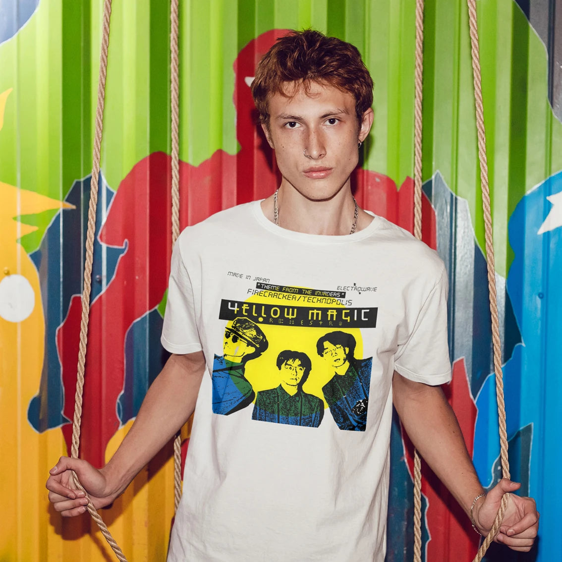 Man wearing a 'Yellow Magic Orchestra' t-shirt in front of a colourful abstract background