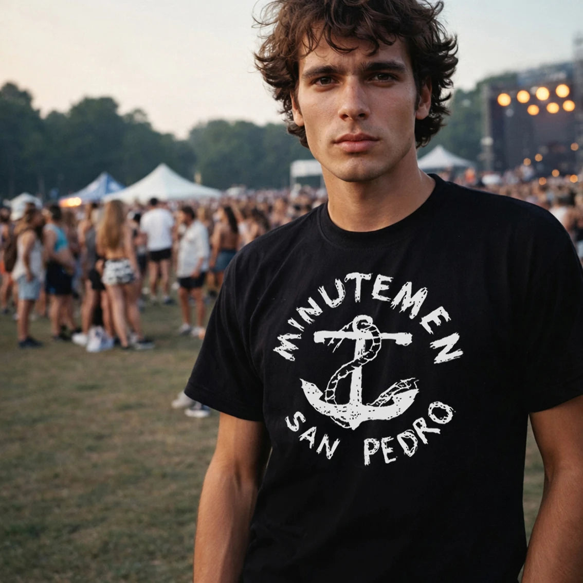 Man wearing a black t-shirt with 'Minutemen San Pedro' design at a festival.