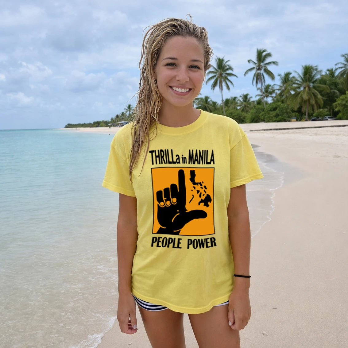 Woman wearing a yellow t-shirt with 'Thrilla in Manila' design on a beach