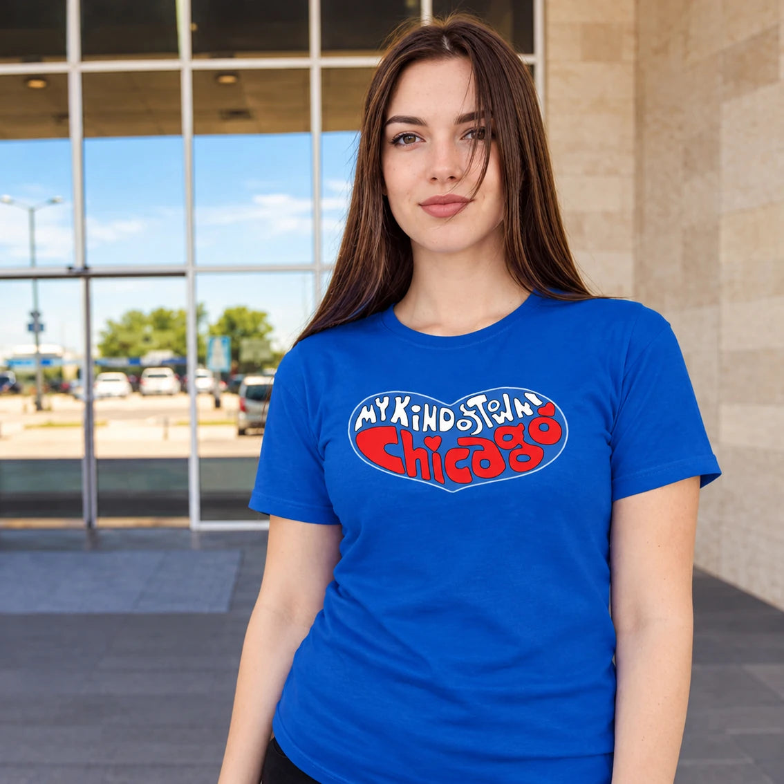 A woman wearing a blue t-shirt with a 'My Kind of Town Chicago' graphic, standing in front of a modern building with large glass windows.