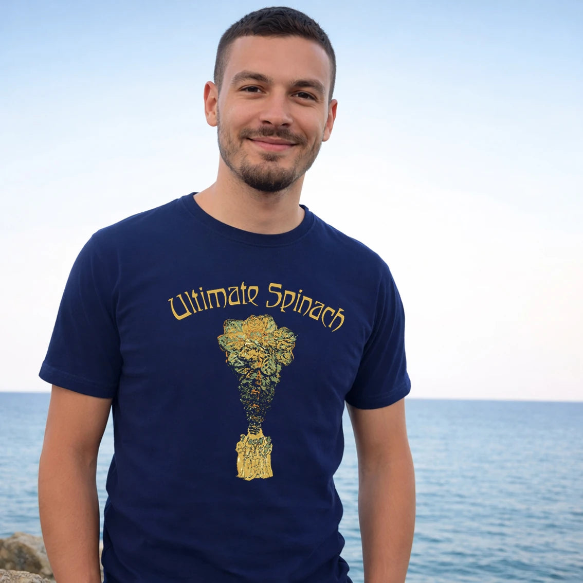 Man wearing a navy blue t-shirt with 'Ultimate Spinach' design by the ocean
