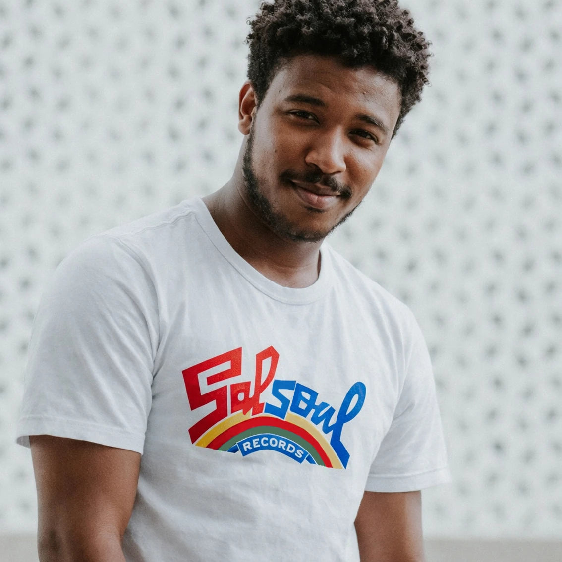Man wearing a white t-shirt with 'Salsoul Records' logo against a textured wall.