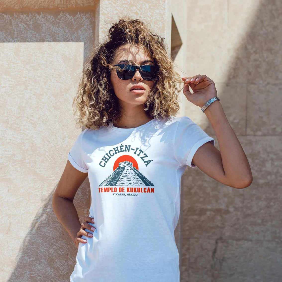 Woman wearing a white t-shirt with Chichen Itza design against a beige wall.