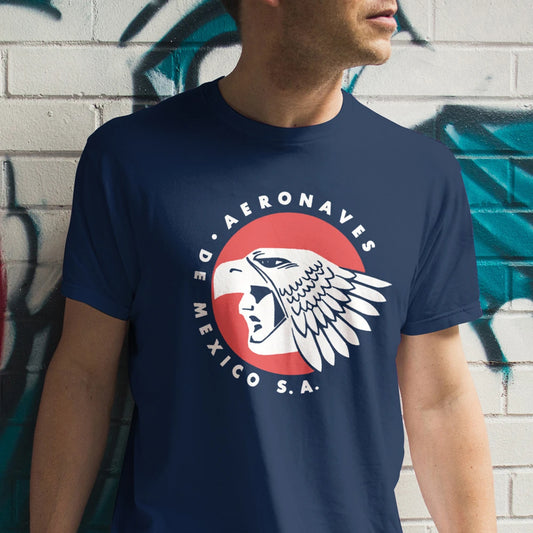 A man is wearing a navy blue t-shirt with a design of an eagle and 'AERONAVES DE MEXICO S.A.' text against a graffiti-covered wall.
