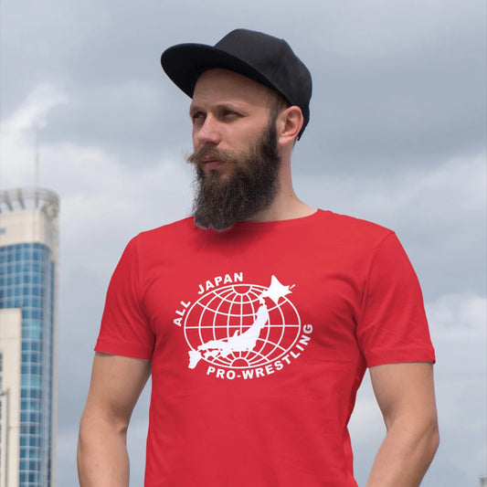 A man in a black cap is wearing a red 'All Japan Pro-Wrestling' t-shirt with a map design on it against a cityscape background.
