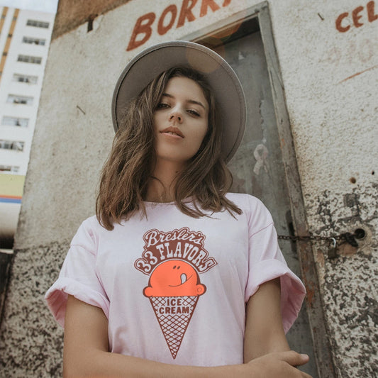 A woman in a hat is wearing a t-shirt with an ice cream cone graphic and text saying Bresler's 33 Flavors, standing against a textured wall.