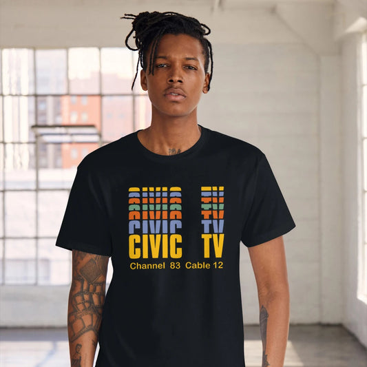 A man is wearing a black t-shirt with colourful 'CIVIC TV - Channel 83 Cable 12' text in a bright indoor setting