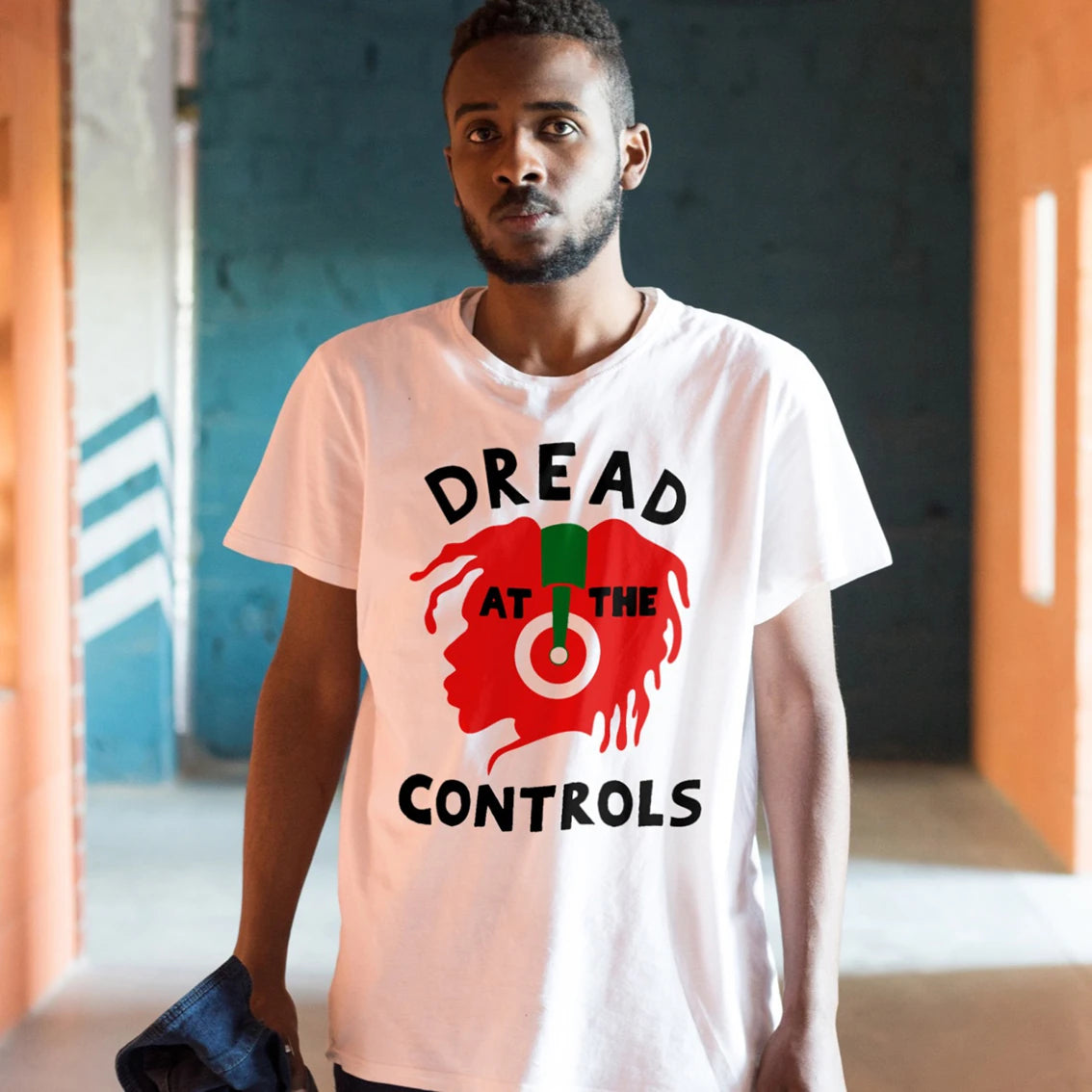 A man is wearing a white t-shirt with a graphic design of the silhouette of the human head and 'DREAD AT THE CONTROLS' text in an indoor setting