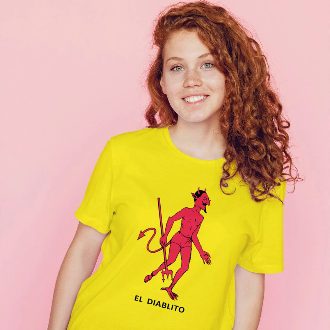 A woman is wearing a yellow t-shirt with a red devil graphic and 'EL DIABLITO' text on a pink background