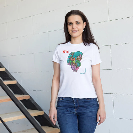 A woman is wearing a white t-shirt with a colorful graphic design with text on the left side saying 'Love' and  'Forever Changes' on the right  against a light brick wall.