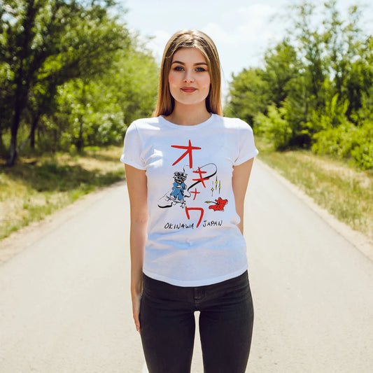 A woman is wearing a white t-shirt with colorful graphics and text saying Okinawa Japan, standing on a sunny road with greenery.