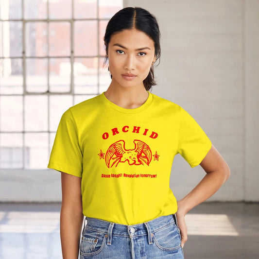 A woman is wearing a yellow t-shirt with red text and graphics saying 'Orchid - Dance Tonight! Revolution Tomorrow!' standing in the room with big window and lots of natural light