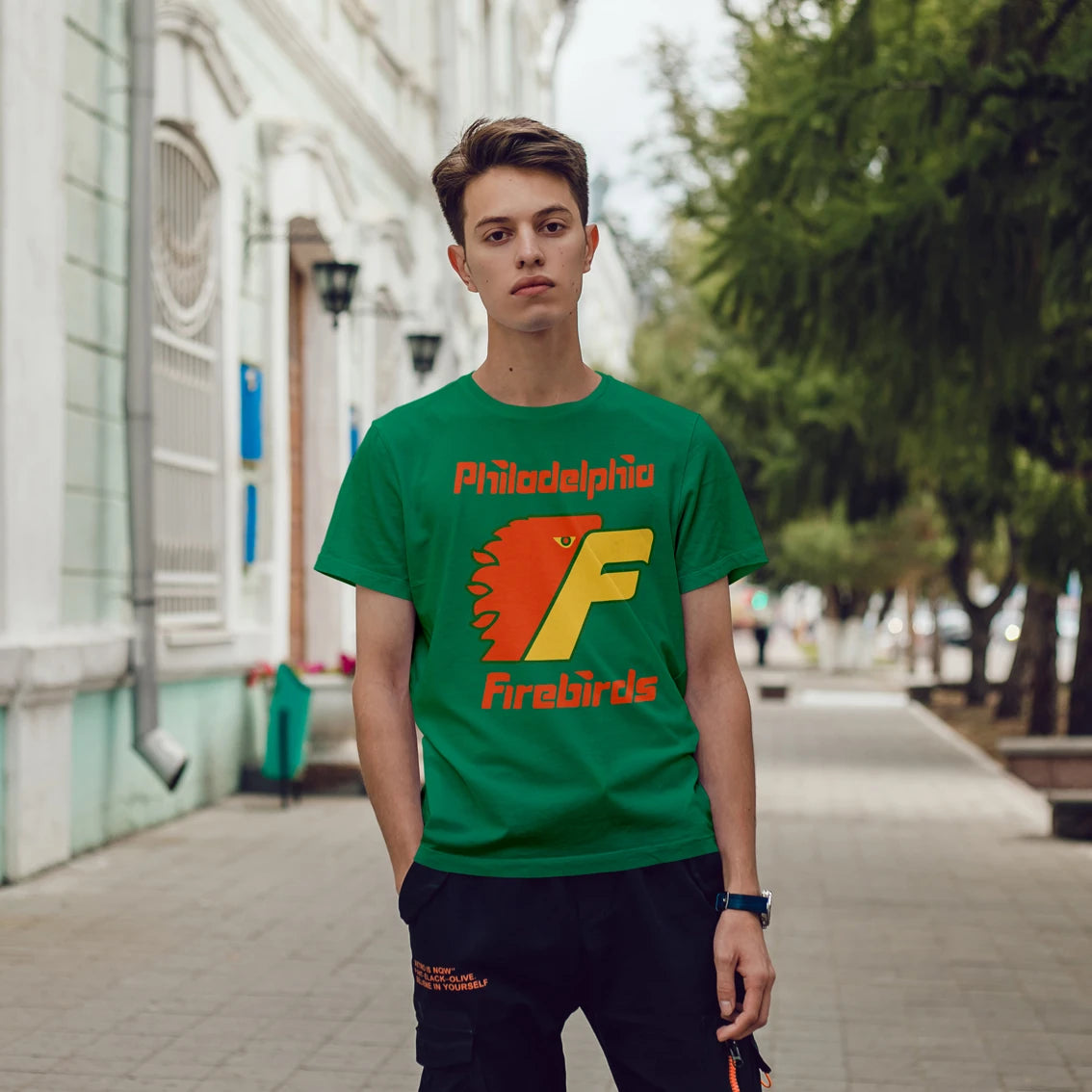 A young man is wearing a green t-shirt with 'Philadelphia Firebirds' design on a city street