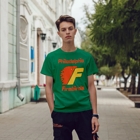 A young man is wearing a green t-shirt with 'Philadelphia Firebirds' design on a city street