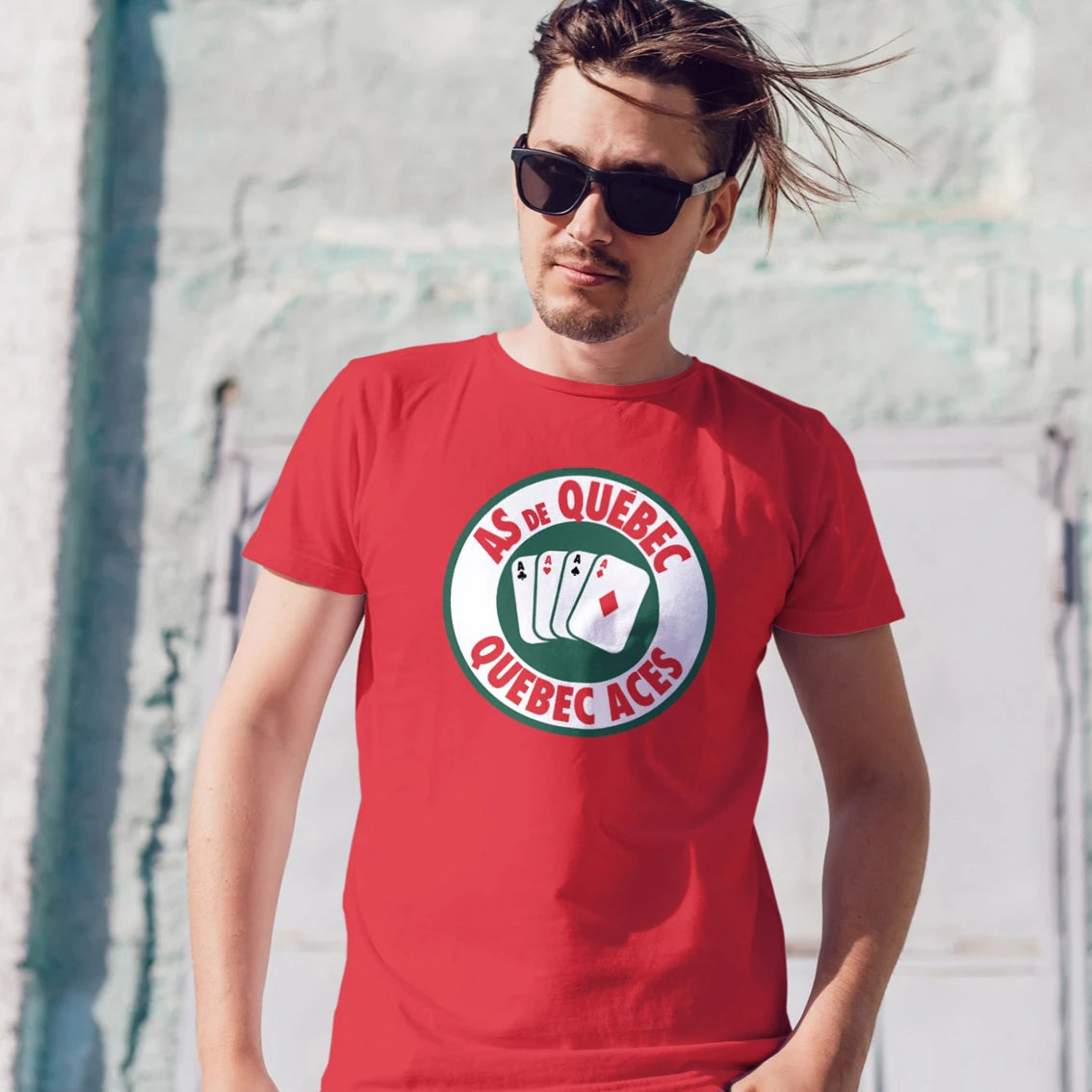 A man in sunglasses is wearing a red t-shirt with a poker cards logo and 'AS DE QUEBEC - QUEBEC ACES' text, standing against a light-colored wall