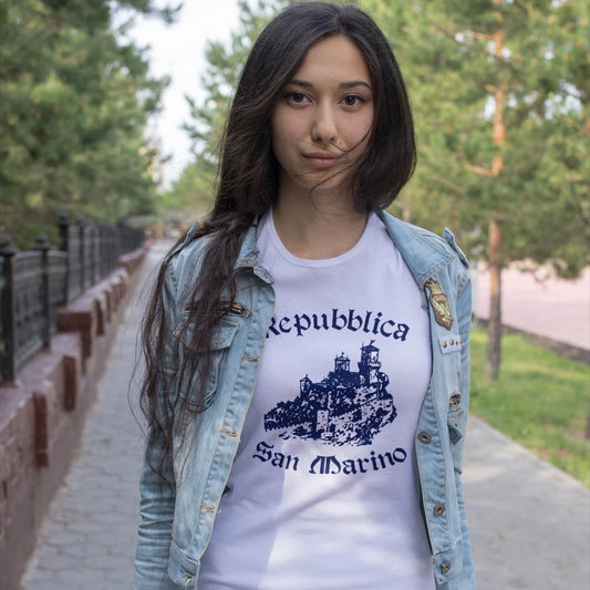 A woman is wearing a white t-shirt with 'Repubblica San Marino' text and design of the castle, standing outdoors.