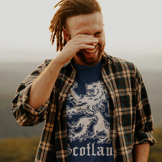 A man is wearing a plaid shirt over a blue t-shirt with a lion design and 'Scotland' text on it, standing outdoors