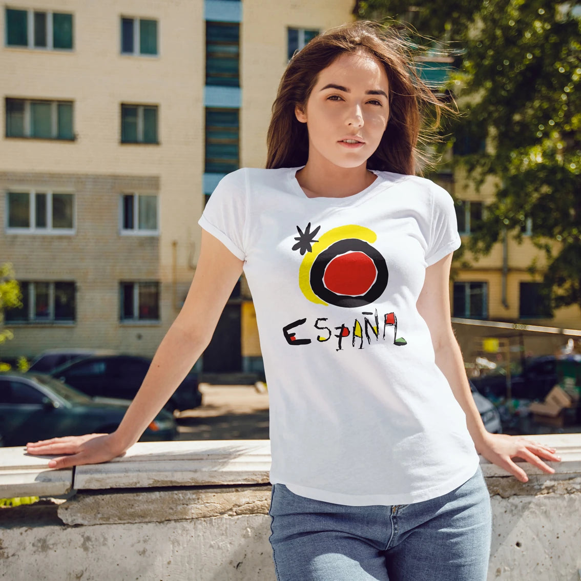 A woman is wearing a white t-shirt with a colorful sunshine design and 'ESPAÑA' text, standing outdoors.