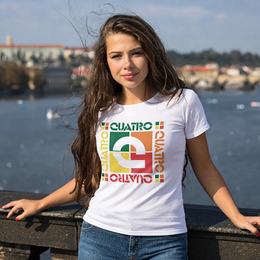 A woman wearing a white graphic t-shirt with a colorful retro design that reads 'QUATRO' in green, yellow, orange, and red, standing outdoors by a body of water with a blurred cityscape background.