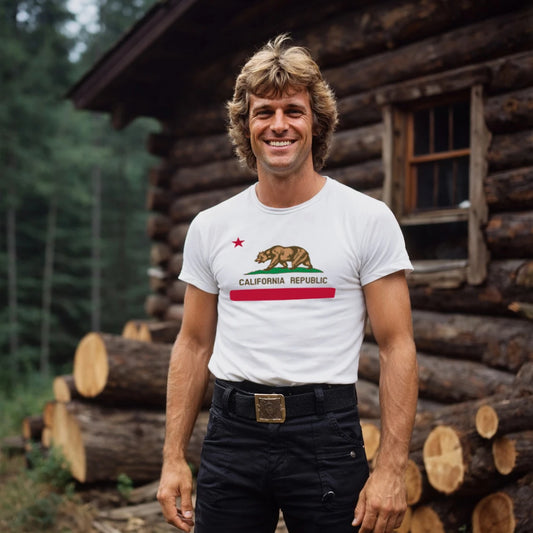 Man wearing a white t-shirt with a bear graphic and 'California Republic' text, standing in front of a log cabin.