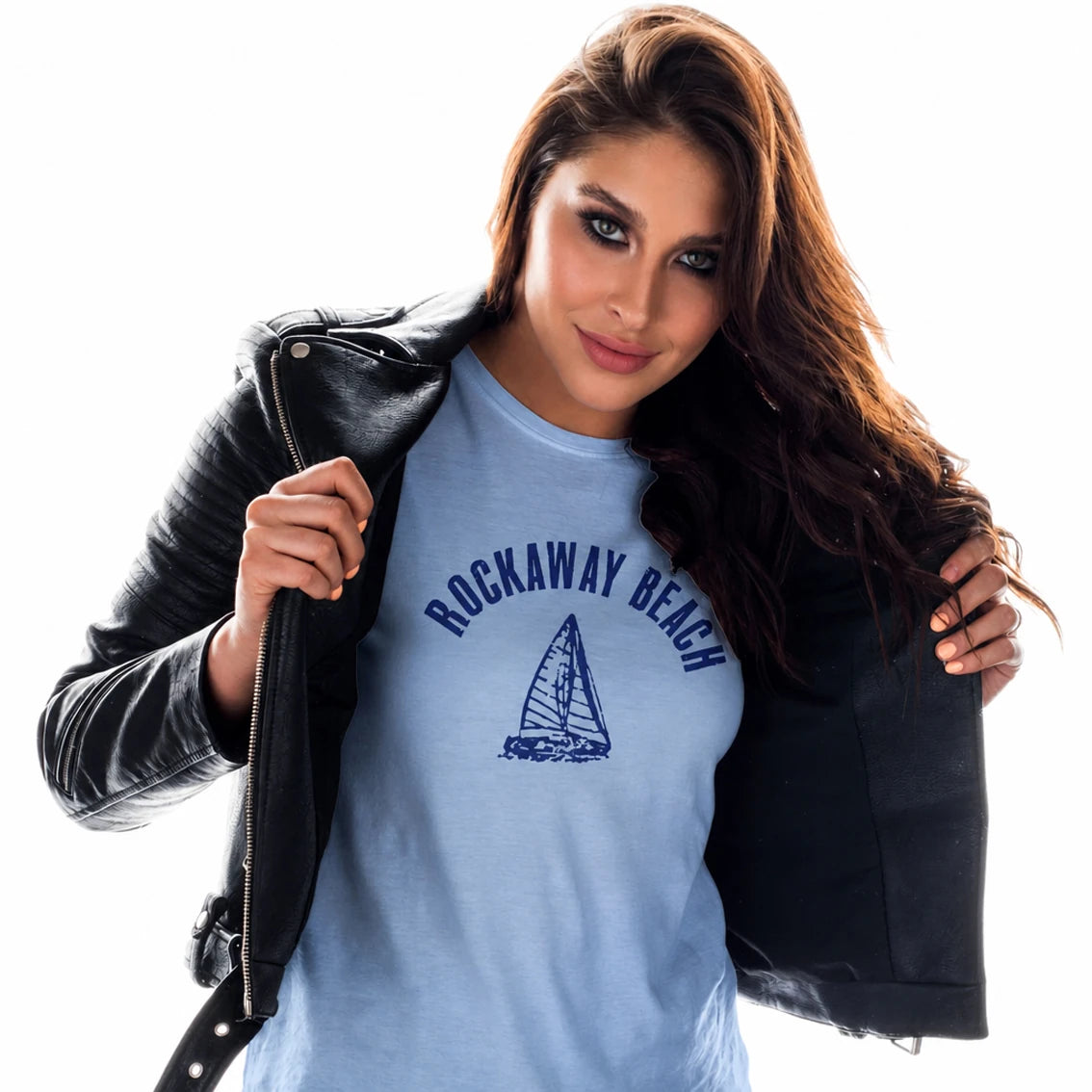 Woman with brown hair wearing a blue t-shirt with the words Rockaway Beach and a sailing boat design, standing in front of a white background