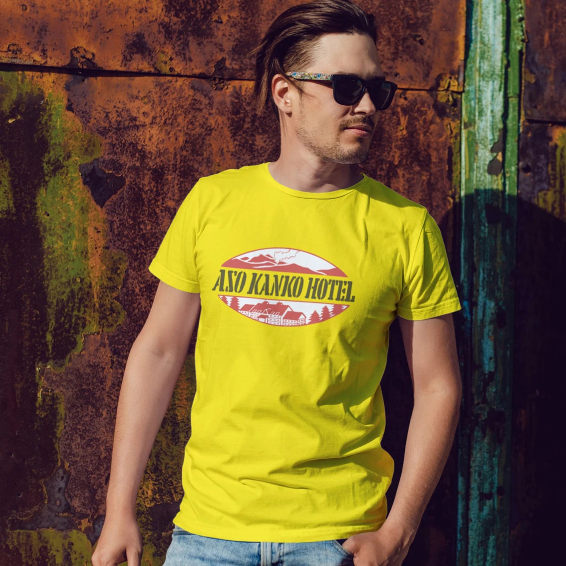 Man wearing a yellow t-shirt with 'AXO KANKO HOTEL' print against a rusty metal wall.