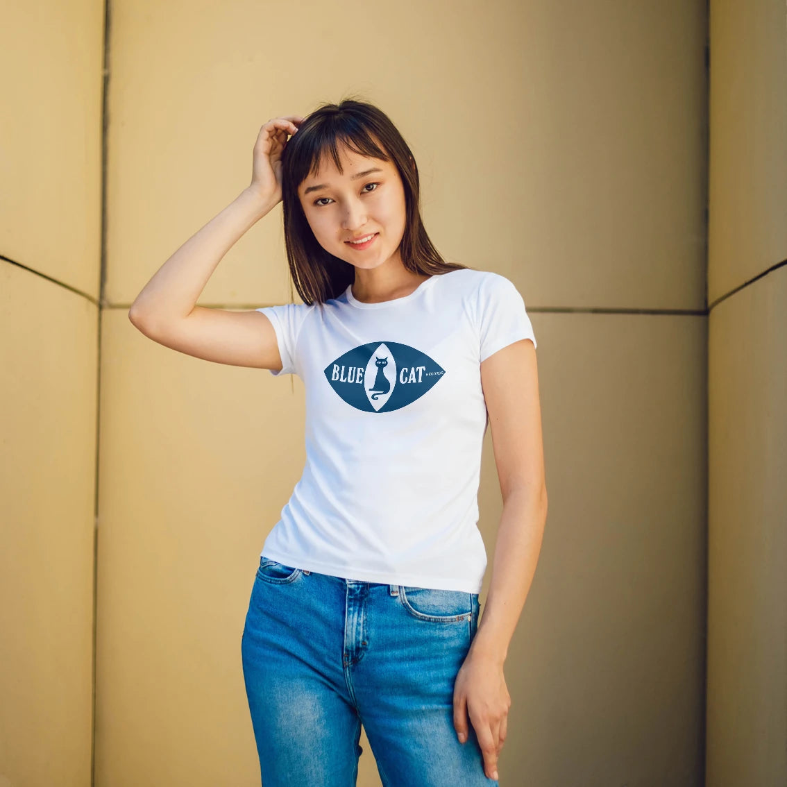 Woman wearing a white t-shirt with a blue cat inside the blue eye logo and 'Blue Cat Records' text against a beige wall