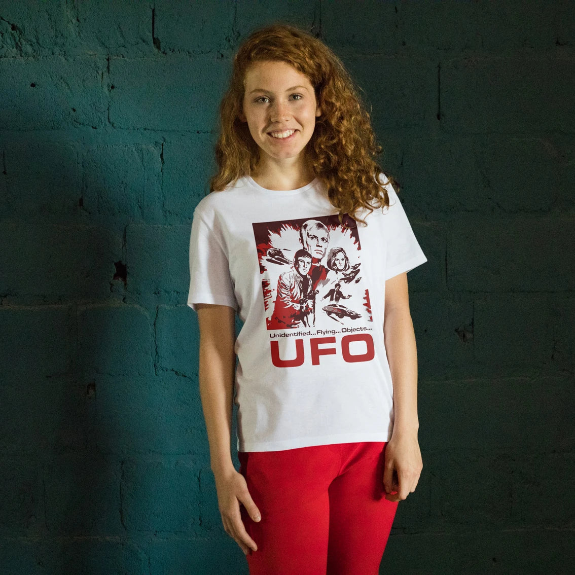Woman wearing a white t-shirt with a graphic design and 'UFO' text against a textured dark wall.