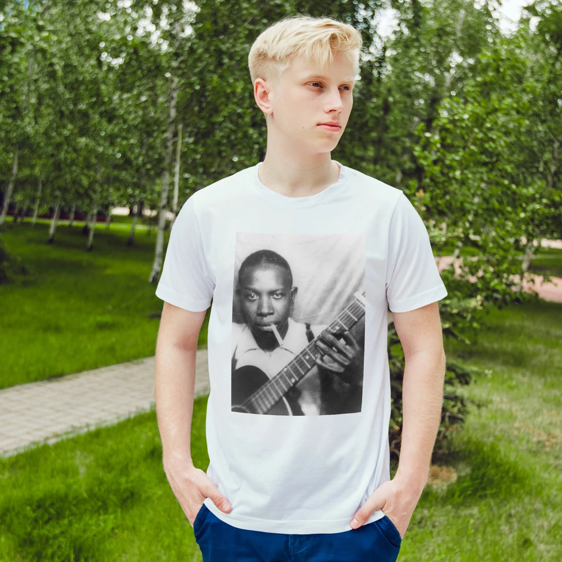 Man wearing a white t-shirt with a graphic of a person playing guitar in a park.