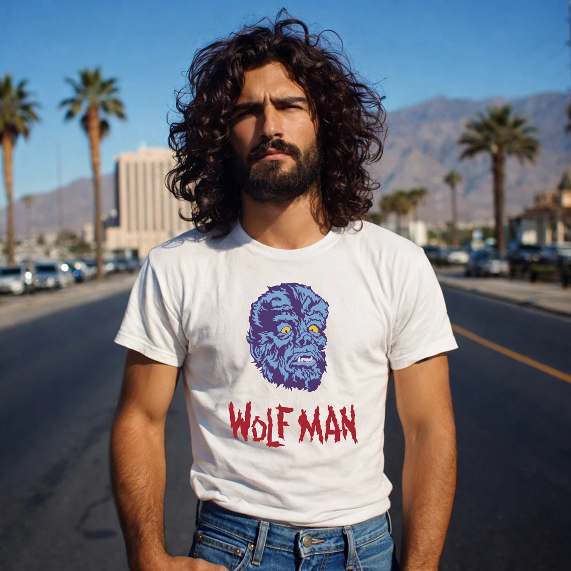 Man wearing a white t-shirt with a graphic design and 'Wolf Man' text, standing on a street with palm trees and mountains in the background.