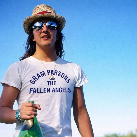 Woman in a hat and sunglasses wearing a 'Gram Parsons and The Fallen Angels' t-shirt holding a bottle with a clear blue sky background