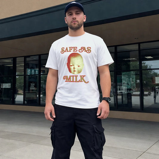 Man in hat wearing a white t-shirt with a baby face graphic design and 'Safe As Milk' text, standing outside a building.