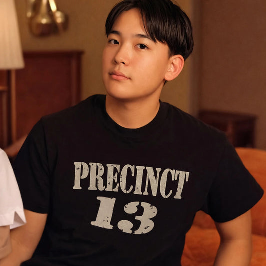 Person wearing a black t-shirt with 'PRECINCT 13' text in a room setting