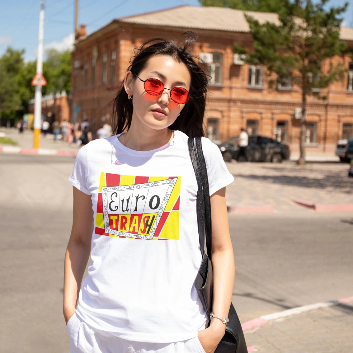 Woman in sunglasses wearing a white t-shirt with colourful 'Eurotrash' text on a street.