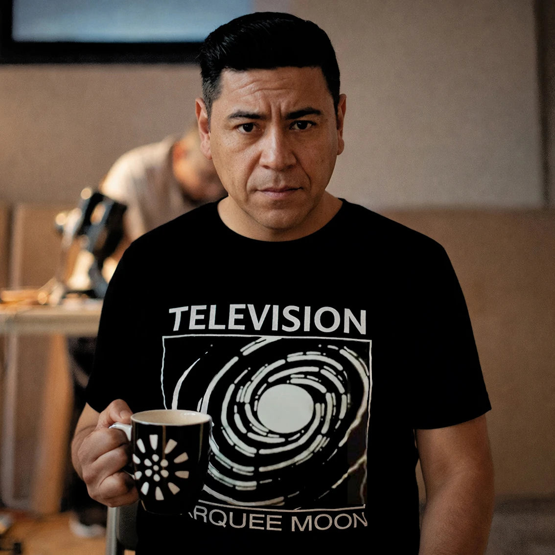 Man wearing a black t-shirt with 'TELEVISION' design, holding a mug.