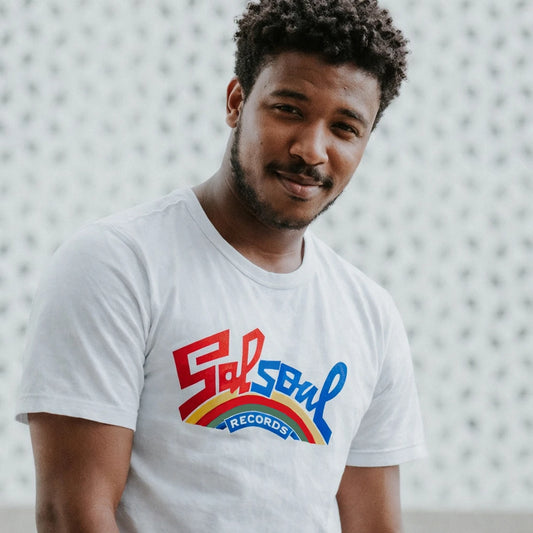 Man wearing a white t-shirt with 'Salsoul Records' logo against a textured wall.