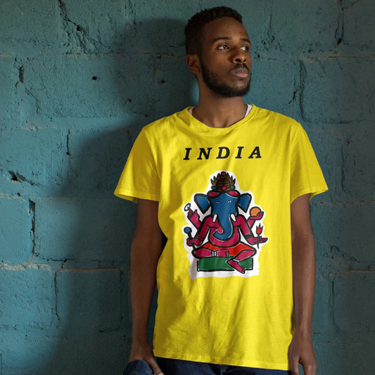 Man wearing a yellow t-shirt with a colorful graphic of elephant-headed Ganesh and 'INDIA' text against a textured blue wall.