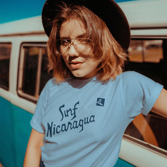 Woman in a hat wearing a 'Surf Nicaragua' t-shirt in front of a vintage van.