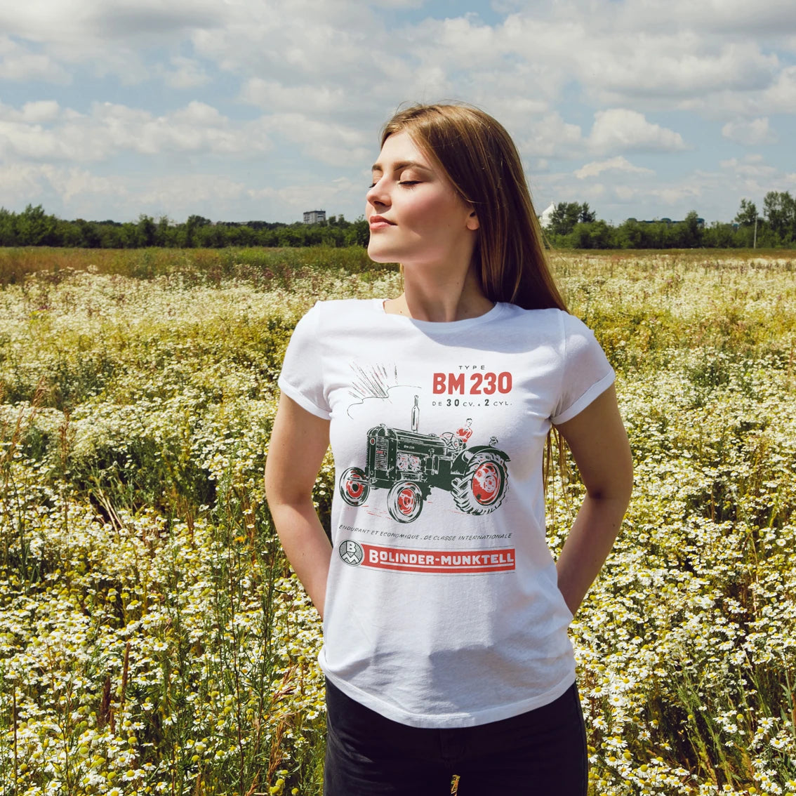 Woman wearing a white t-shirt with a tractor design and text saying 'Bolinder-Munktell' in a field