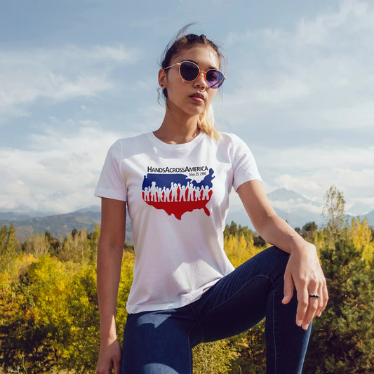 A woman in sunglasses wearing a 'Hands Across America' t-shirt outdoors with trees and sky in the background