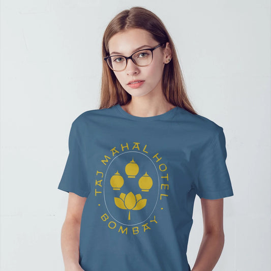 A woman in glasses is wearing a blue t-shirt with 'Taj Mahal Hotel, Bombay' design on a white background