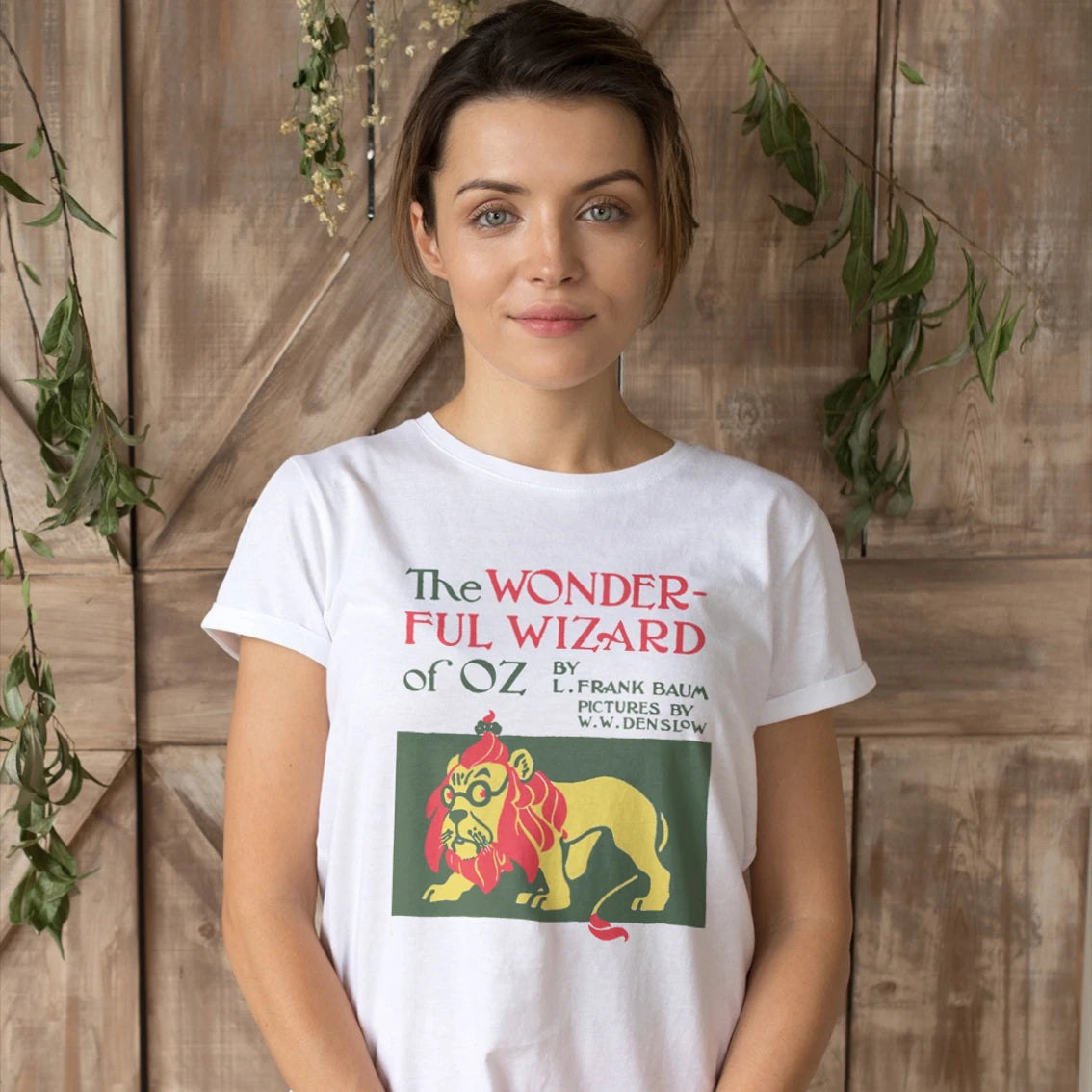 A woman is wearing a 'The Wonderful Wizard of Oz' t-shirt with lion illustration on it against a wooden background