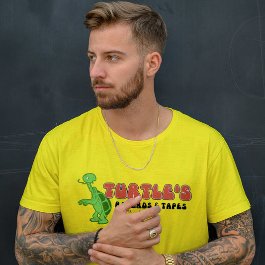 A man is wearing a yellow t-shirt with a graphic design of a turtle and 'TURTLE'S RECORDS & TAPES' text, standing against a dark background.